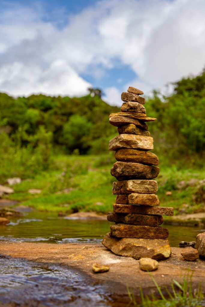Vertical stack of stones creating a cairn by a calm river in a lush forest setting.